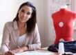 A female sole company owner and director working at a desk in her fashion business with a tailor's dummy in the background.