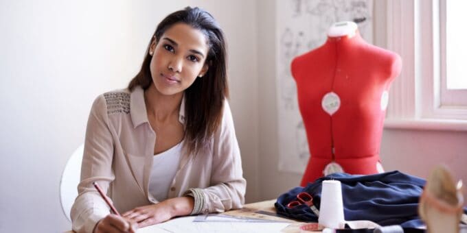 A female sole company owner and director working at a desk in her fashion business with a tailor's dummy in the background.