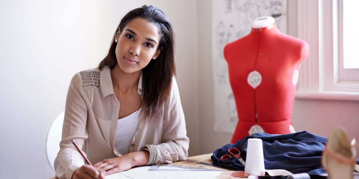 A female sole company owner and director working at a desk in her fashion business with a tailor's dummy in the background.