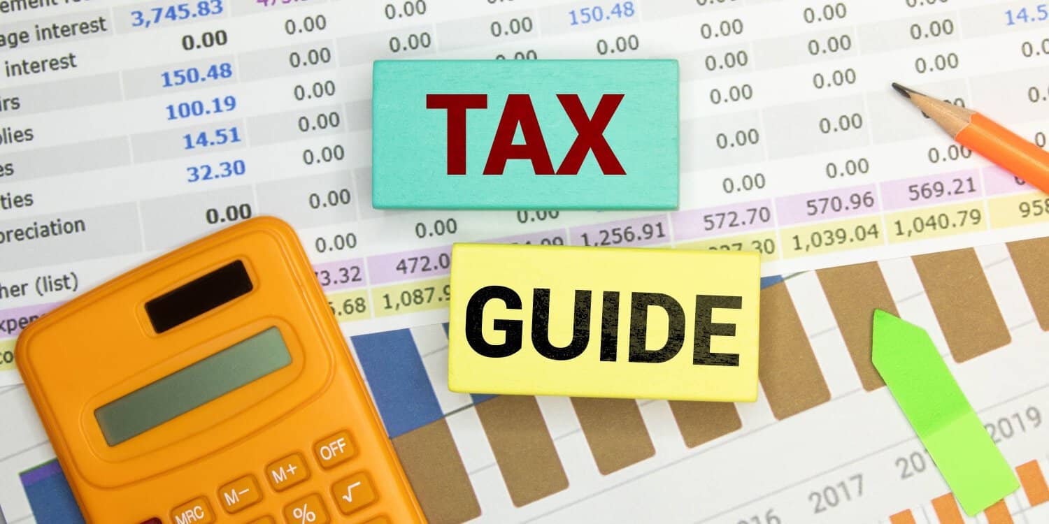 TAX GUIDE text on a notebook with pencil, calculator, and folder on a chart background.