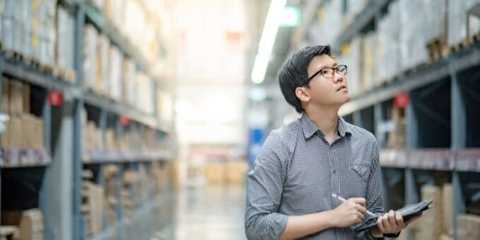 Asian business owner doing a stock take in his warehouse using a digital tablet and pen.