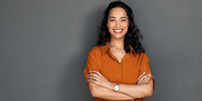 Portrait of a young female entrepreneur exuding confidence with pleasant smile and crossed arms isolated on grey wall with copy space.