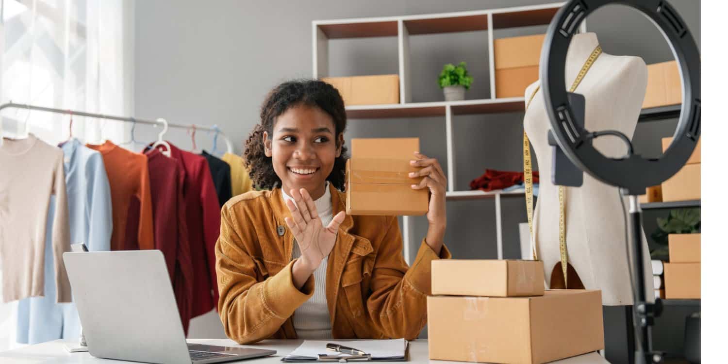 Female small business owner working at home selling her products online and recording a video with her phone and ring light.