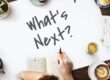 An overhead shot of a new business owners' meeting with a white sheet of paper in the centre of the table with the phrase 'What's Next?' written with a black marker pen.
