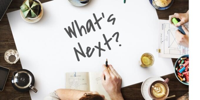An overhead shot of a new business owners' meeting with a white sheet of paper in the centre of the table with the phrase 'What's Next?' written with a black marker pen.
