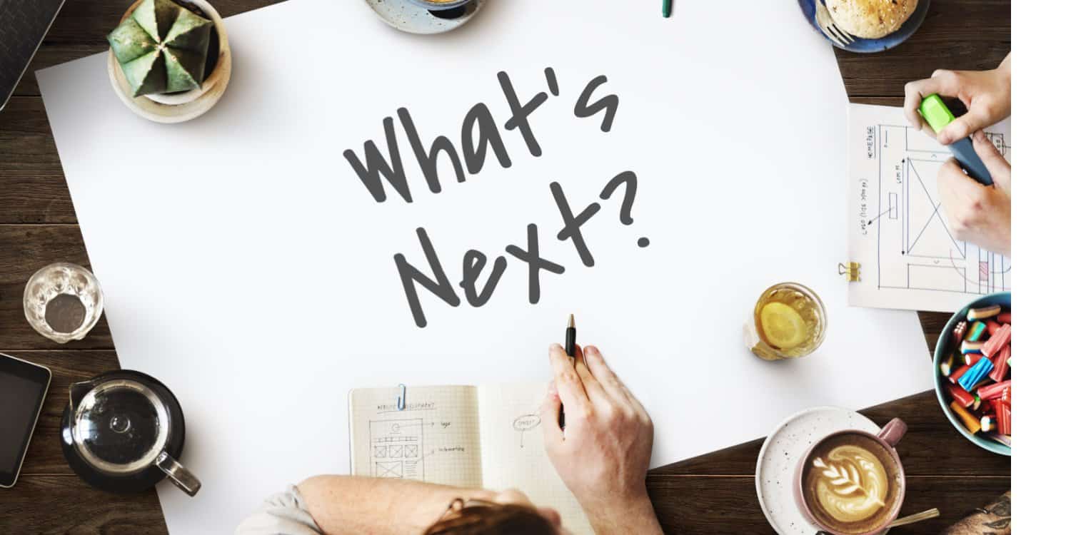 An overhead shot of a new business owners' meeting with a white sheet of paper in the centre of the table with the phrase 'What's Next?' written with a black marker pen.