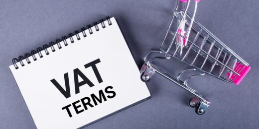 A miniature shopping cart lying next to a white notepad with VAT TERMS written on it in black font.