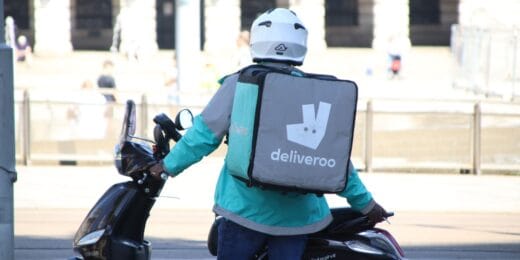Deliveroo scooter driver, working under a zero-hours contract, waits in the sun for his next order.