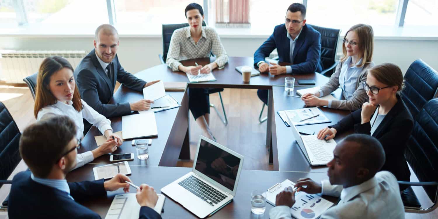 Eight shareholders in business suits sitting at a boardroom table in a shareholders' meeting.