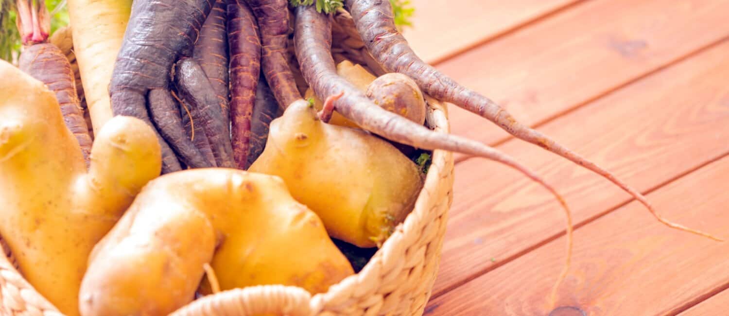 A selection of imperfect carrots and potatoes in a wicker basket, highlighting the importance of reducing food waste