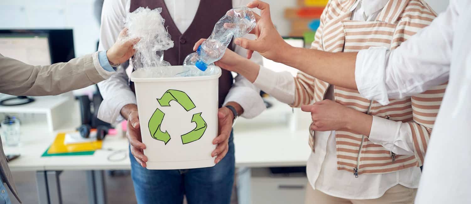 Colleagues dropping plastic recycling into a bin at work.