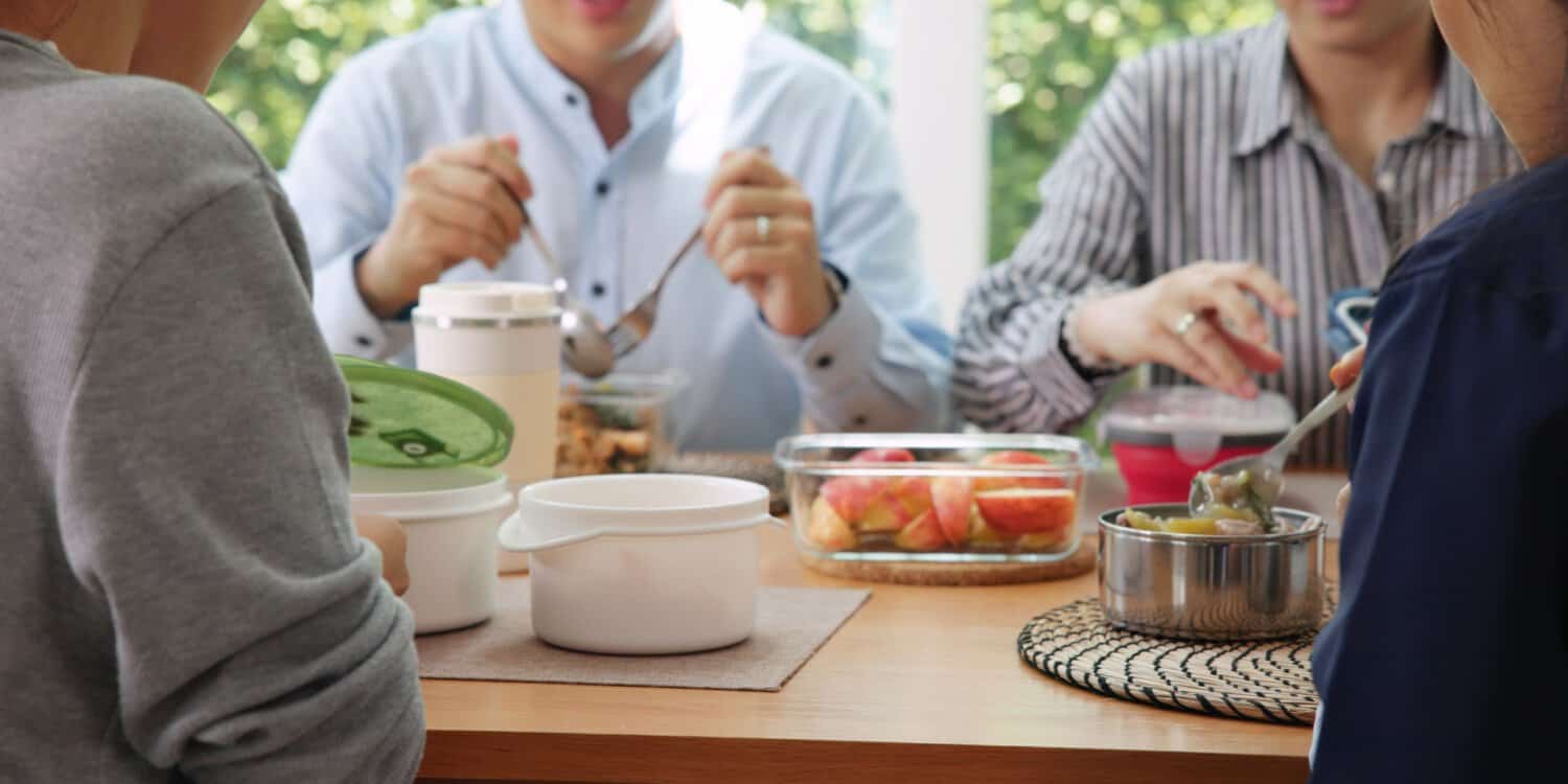 A group of workers enjoying their lunch at a wooden table in a modern office.