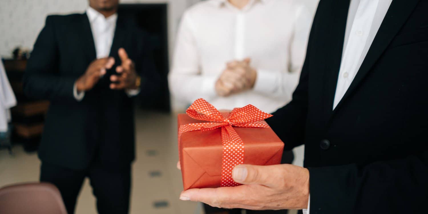 A limited company director in a suit gives an employee a trivial benefit wrapped in a red box
