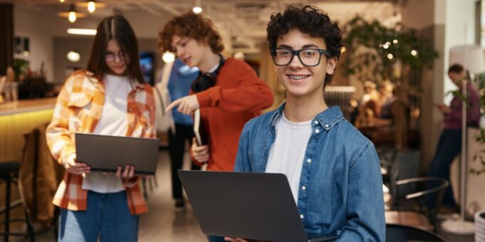 Group of teenagers using laptops in a modern workspace, showing young people under 18 exploring ideas and taking steps to start a company at an early age