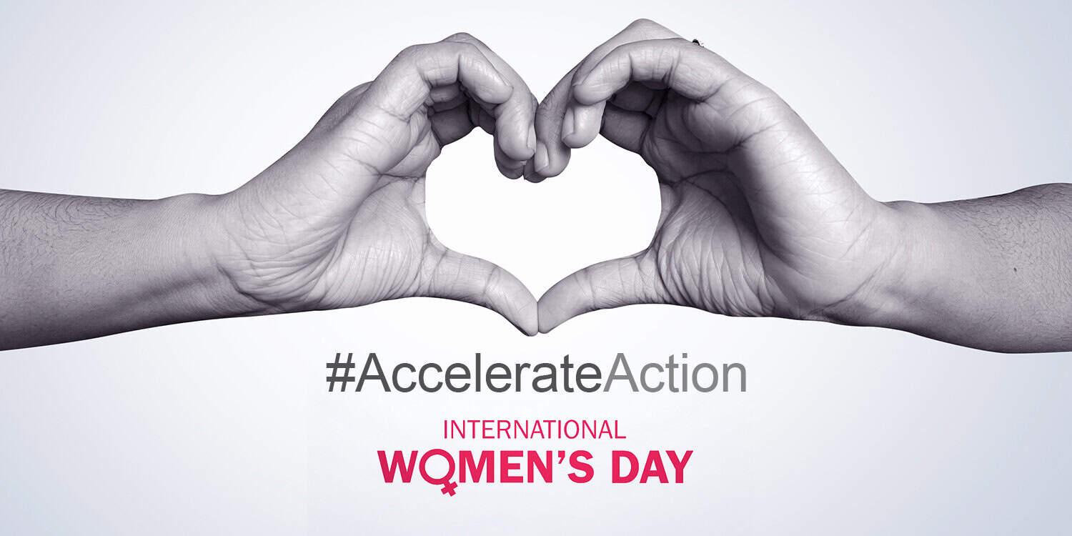 A black and white image of two hands connected to make a heart shape. Underneath them, the text reads '#AccelerateAction' in grey and 'International Women's Day' in pink