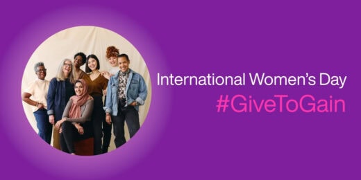 Group portrait of diverse women smiling together, celebrating International Women's Day with the phrase “#GiveToGain” on a purple background.