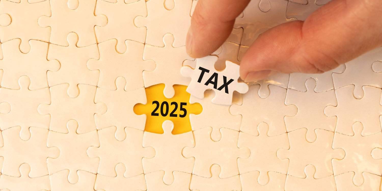 Concept words '2025 TAX' on beautiful white jigsaw puzzle, with male hand holding jigsaw piece.