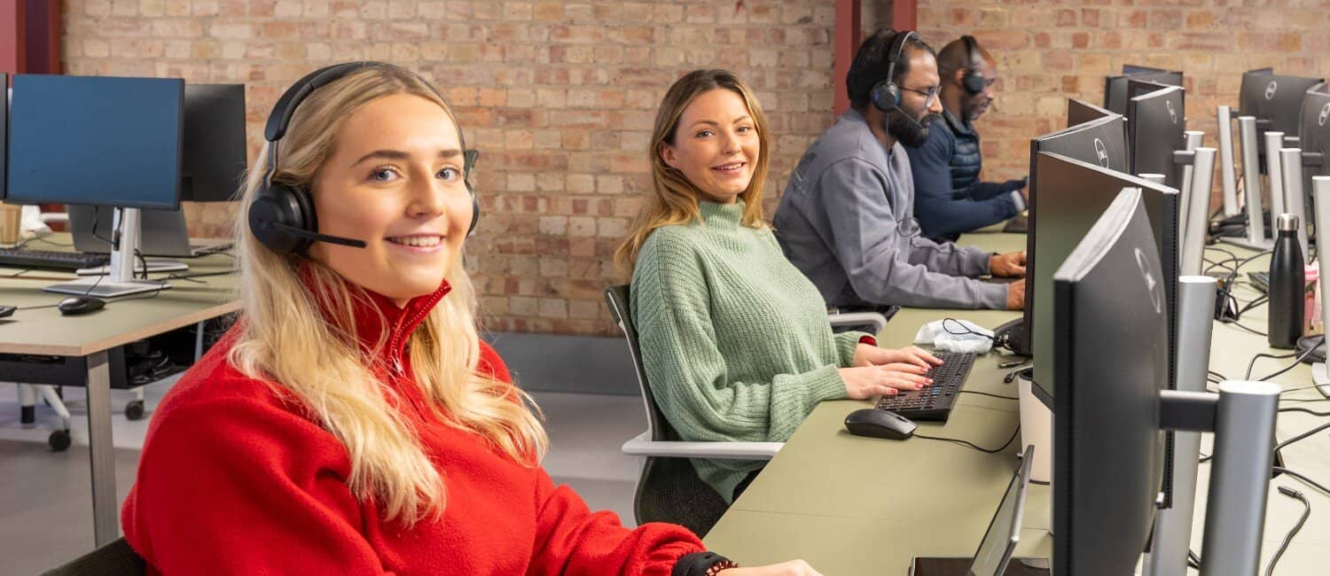 Account managers sitting at their desks in front of computer monitors, smiling towards the camera in a modern office