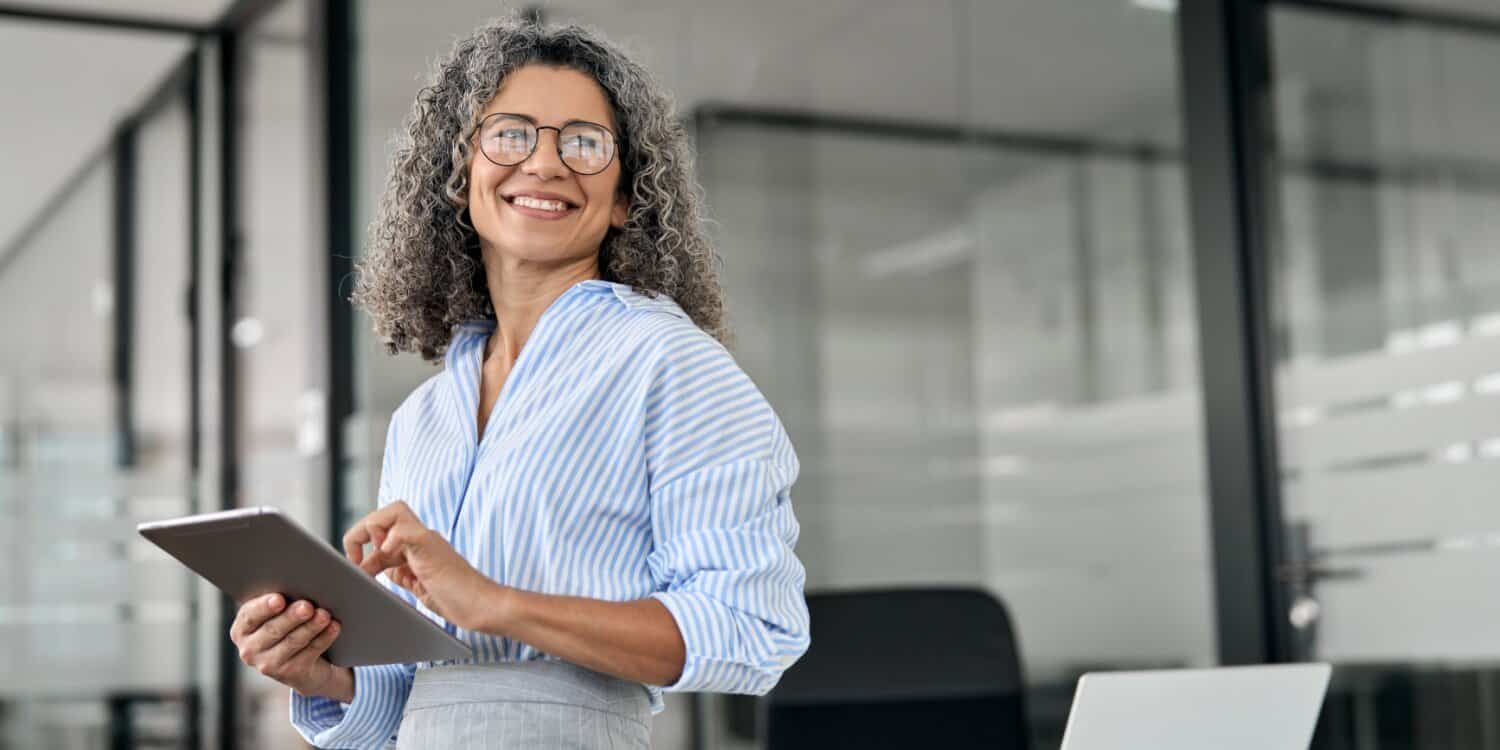 Portrait of smiling mature female solopreneur with tablet standing in her office.