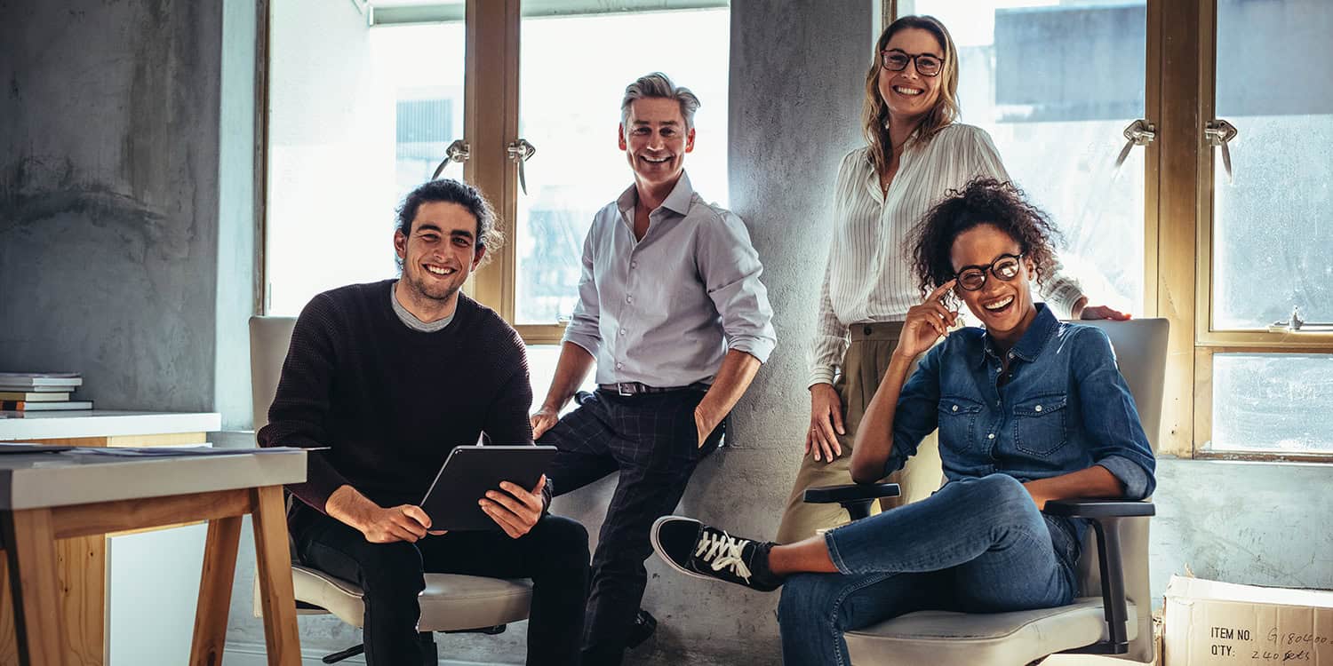 Smiling team of four in a bright office, reflecting growth from solopreneur to small business.