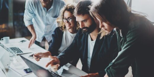 A team of young professionals collaborating around a laptop in a modern office, illustrating teamwork and innovation in a startup environment.