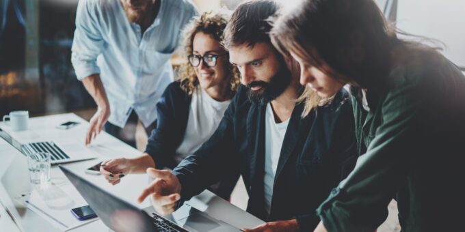 A team of young professionals collaborating around a laptop in a modern office, illustrating teamwork and innovation in a startup environment.