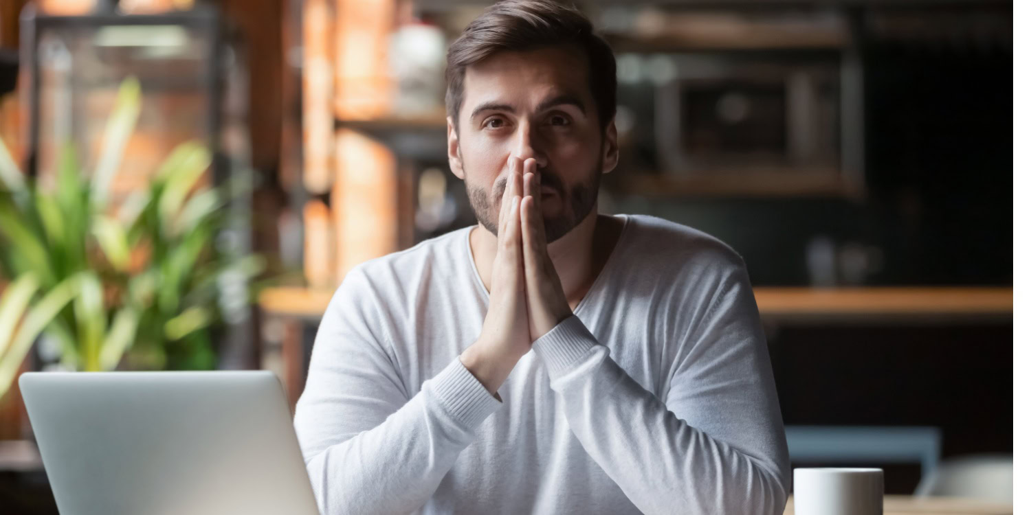 Thoughtful businessman sitting a desk with hands in prayer position pondering the stages of the business cycle.