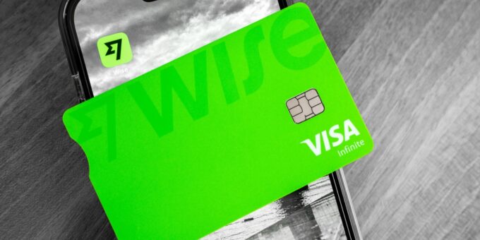 A vibrant green Wise Visa Infinite debit card rests on a smartphone displaying the Wise app logo against a monochrome background.