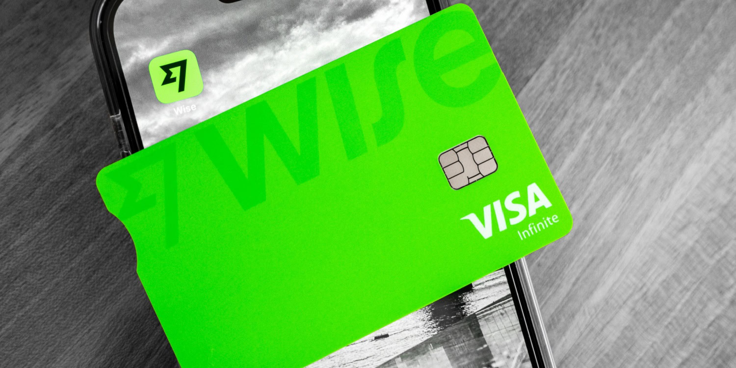 A vibrant green Wise Visa Infinite debit card rests on a smartphone displaying the Wise app logo against a monochrome background.