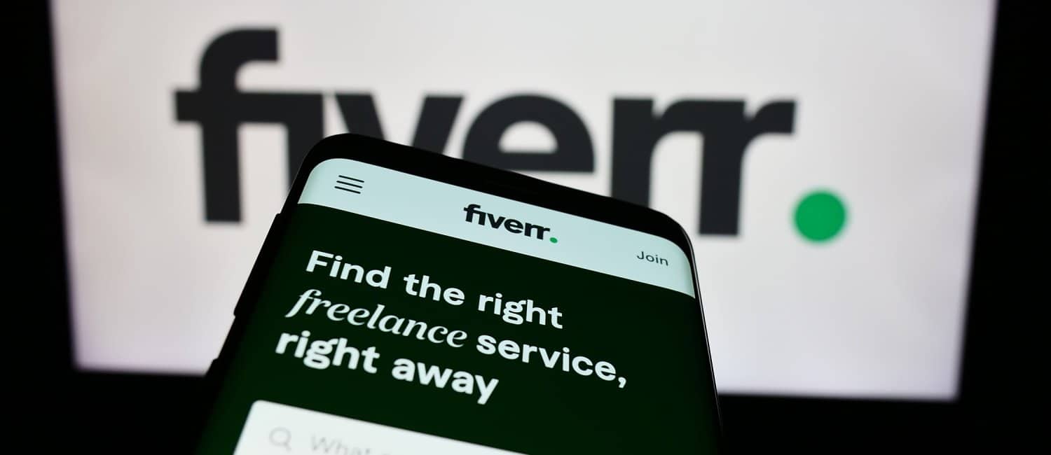 A smartphone help in front of a laptop screen with website of freelance platform company displayed on laptop and phone.