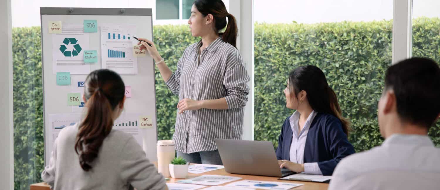 A business owner presents her ideas on sustainability reporting to engaged colleagues in a bright, modern office setting.