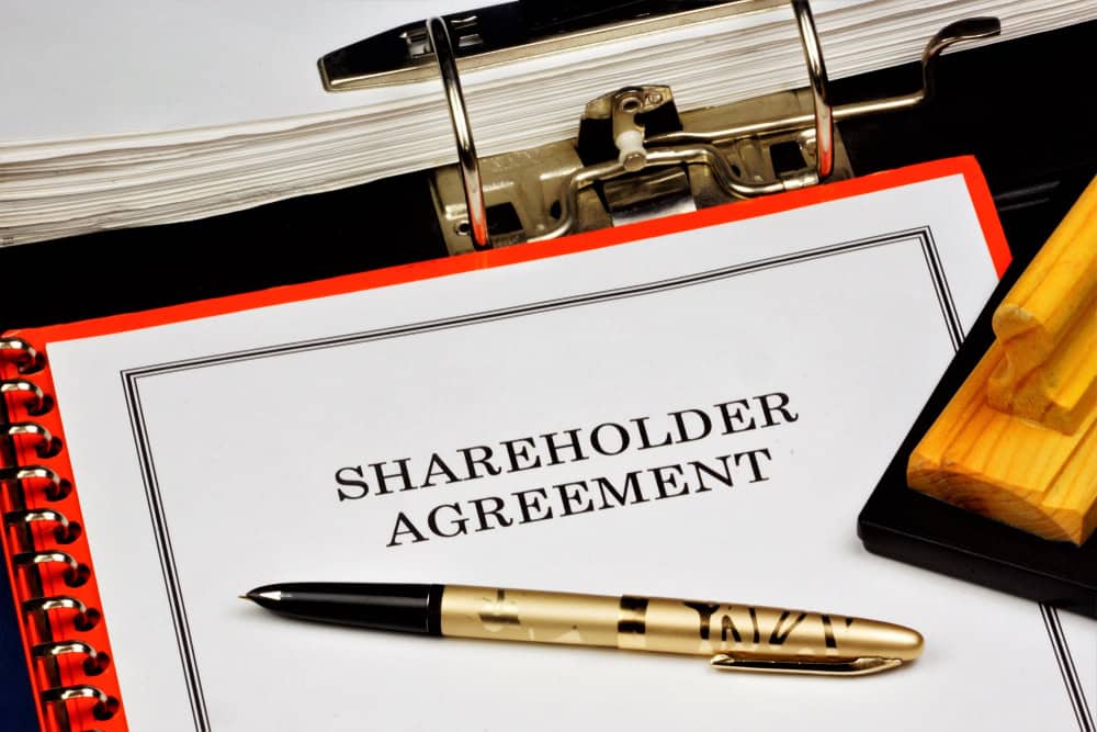 A clipboard holding a white paper document with the words 'Shareholder Agreement' printed on the front.