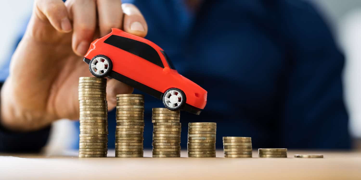 Conceptual image illustrating depreciation in business, showing a hand moving a toy car down a staircase of stacked coins, symbolising the decreasing value of an asset over time