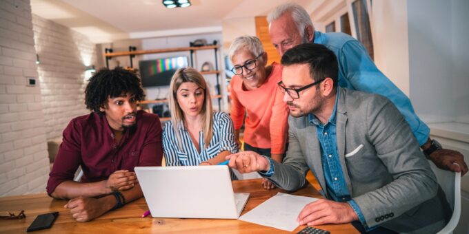 Five family members, young to elderly, gathered around a laptop, intently discussing business matters.