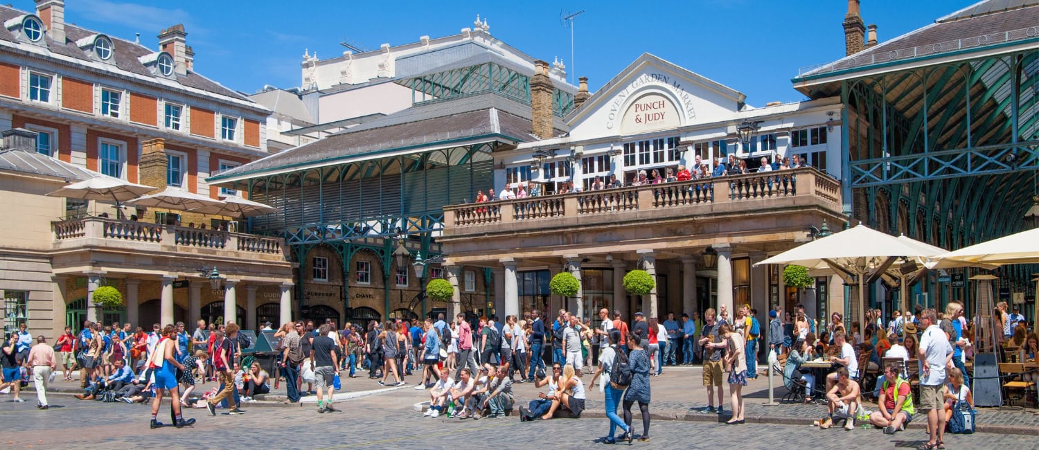 Busy scene at Covent Garden Market in London with crowds of people enjoying the sunny day outside shops and cafes.