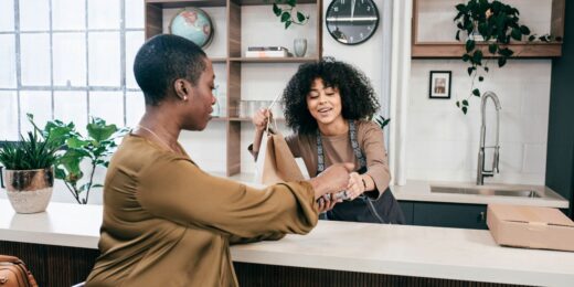 Customer pays for takeout as a café employee hands over a paper bag and processes a card payment refund at the counter