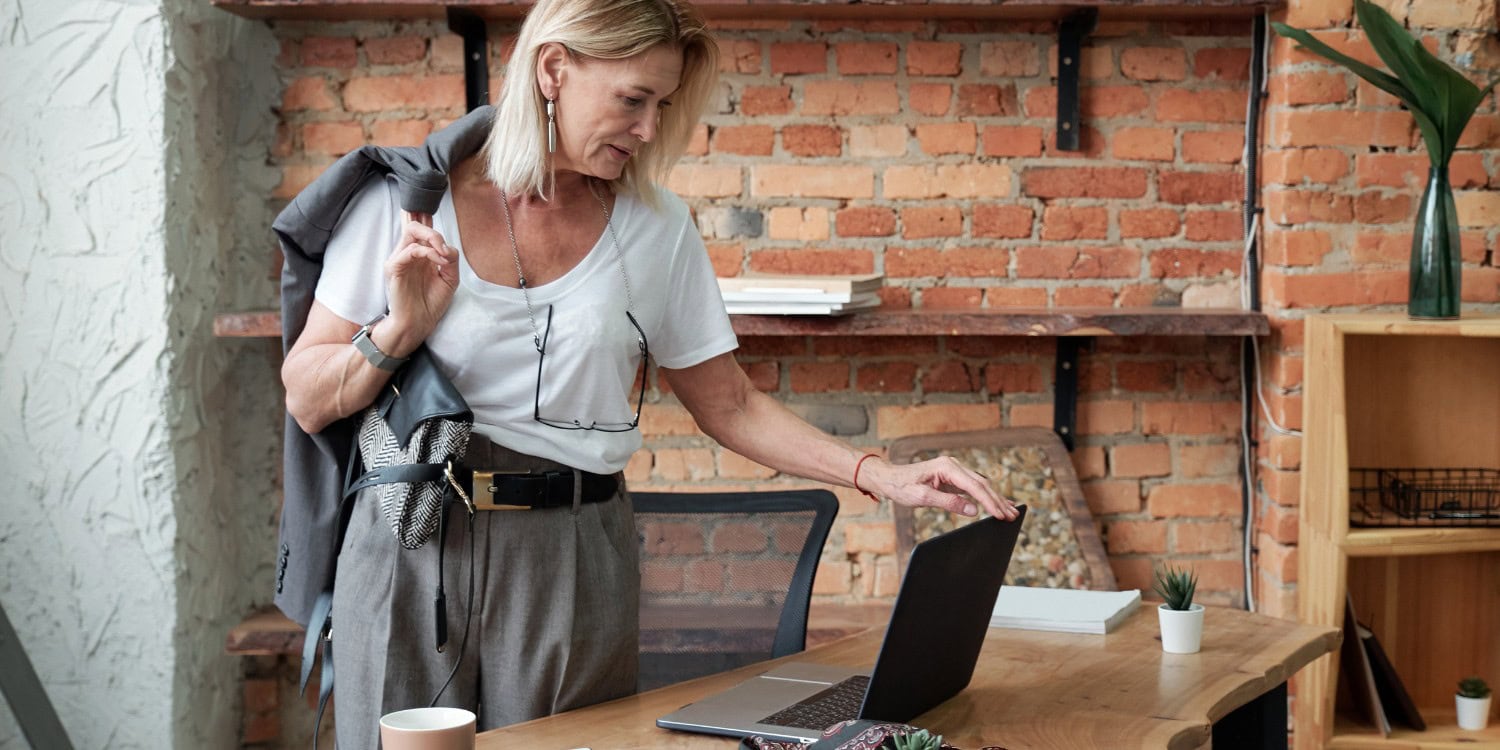 A woman standing next to her desk and closing her laptop.