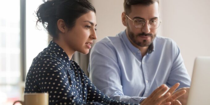 A businesswoman mentoring a male entrepreneur, pointing something out on a laptop screen while he listens attentively during their meeting.