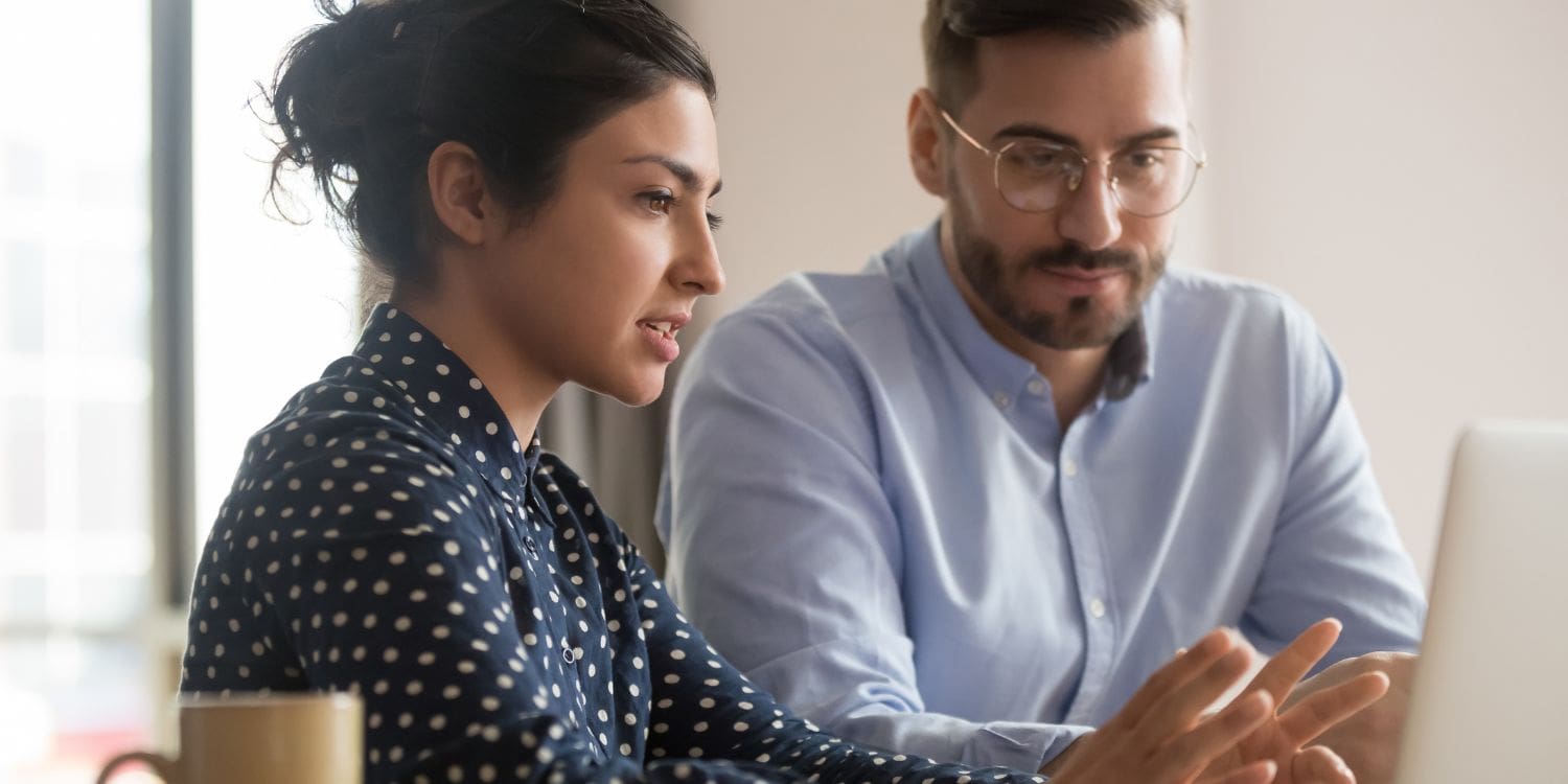 A businesswoman mentoring a male entrepreneur, pointing something out on a laptop screen while he listens attentively during their meeting.