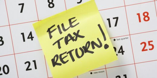A yellow sticky note reading "File tax return!" stuck on a calendar page, as a reminder of upcoming tax dates and deadlines.